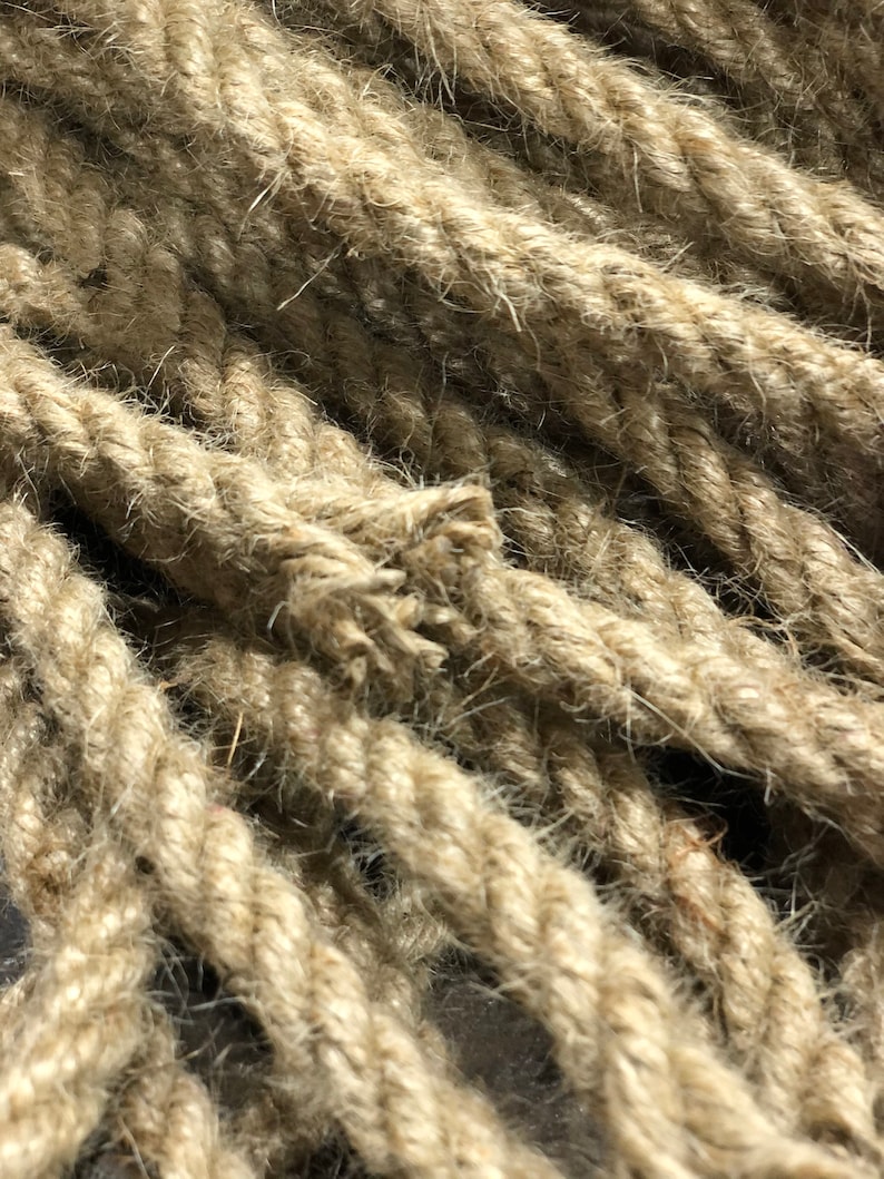 May include: Close-up of thick, natural-colored rope. The rope is tightly twisted, with visible fibers and a slightly frayed end. The texture appears rough and durable, suggesting a nautical or rustic theme.