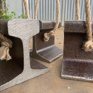 May include: Three metal bookends with a rustic, industrial design. Each bookend is shaped like a section of a railroad track and features a natural rope handle. The bookends have a weathered, textured appearance with shades of gray and brown.