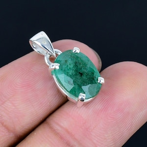 Può includere: Un ciondolo d'argento con una grande pietra di smeraldo di forma ovale. Lo smeraldo è di colore verde scuro e ha una taglio sfaccettato. Il ciondolo è incastonato in una montatura a bezel d'argento con quattro griffe.