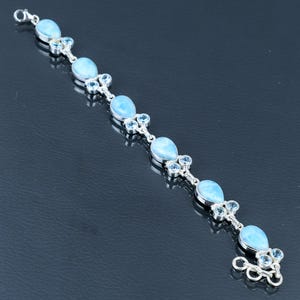 Peut inclure: Un bracelet en argent orné de pierres bleues claires en forme de goutte d'eau, entrecoupées de groupes de petites pierres bleues claires rondes. Le bracelet a un design délicat et orné.