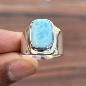 May include: A silver ring featuring a light blue gemstone. The gemstone is rectangular in shape with a smooth, polished finish.