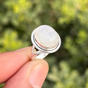 Könnte beinhalten: Ein silberner Ring mit einem weißen, ovalen Mondstein. Der Ring hat ein zartes, durchbrochenes Design.