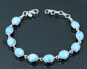 Puede incluir: Una pulsera de plata con piedras preciosas ovaladas de color azul claro. Las piedras están unidas por eslabones de cadena de plata. La pulsera se muestra sobre una superficie oscura, resaltando el diseño y el color de la joya.