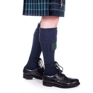 Op de afbeelding: Een paar donkerblauwe wollen kiltkousen met groene bies, gedragen met zwarte leren veterschoenen.