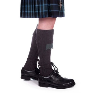 May include: A pair of dark gray wool kilt hose with a green trim. The hose are worn with black leather shoes.