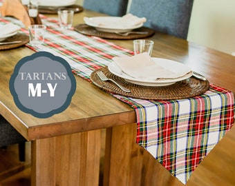 May include: A red, white, and blue plaid table runner with the text "TARTANS M-Y" on a wooden table with place settings.