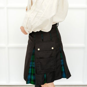 May include: A black kilt with a green and blue tartan pattern. The kilt has a large cargo pocket on the front and two gold buttons.