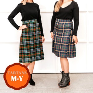 May include: Two women wearing black long-sleeved shirts and tartan kilts. The kilts are green, blue, and yellow with a plaid pattern. The women are standing on a white background. The text "TARTANS M-Y" is in a circle on the bottom left of the image.