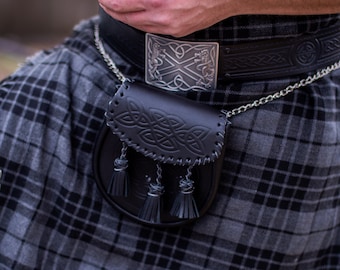 May include: A black and gray plaid kilt with a black leather belt and a silver buckle. A black leather sporran with a Celtic knot design hangs from the belt.