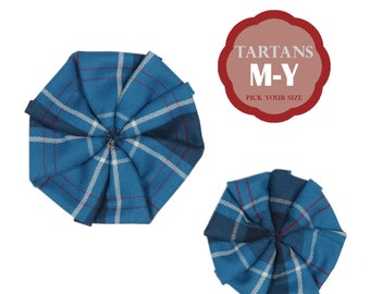 Può includere: Due rosette in tessuto tartan blu e bianco, una più grande dell'altra. Le rosette sono piegate in forma circolare. Il testo "TARTANS M-Y PICK YOUR SIZE" è in un cerchio rosso sopra le rosette.