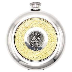 Può includere: Una fiaschetta in acciaio inossidabile con tappo argentato e centro dorato. Il centro presenta un emblema dettagliato con la scritta "NE OBLIVISCARIS" in un design circolare. La fiaschetta ha una superficie lucida e riflettente.
