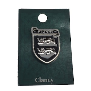May include: A silver-coloured Clancy family crest badge with a black background and two silver lions. The badge is on a dark green card with the name "Clancy" printed at the bottom.
