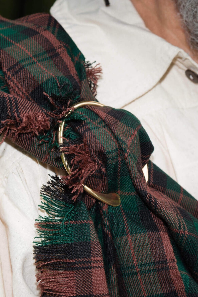 May include: A green, black, and brown plaid kilt with a gold metal kilt pin.