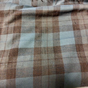 May include: A close-up of a brown and blue plaid fabric. The fabric has a woven texture and is folded in the center.
