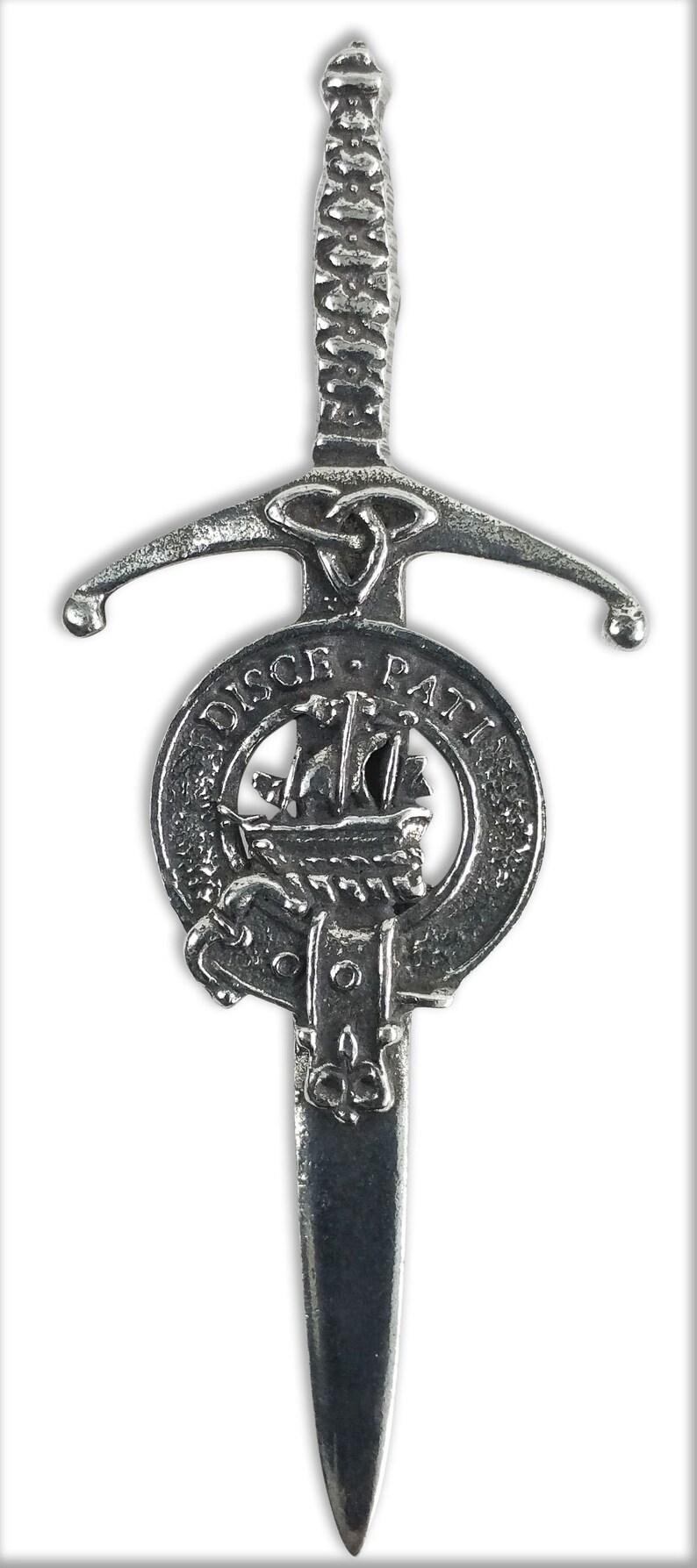 May include: A silver-toned kilt pin in the shape of a sword with a Celtic knot design. The sword is attached to a round shield with the words "DISCE. PATRI" and a ship design.