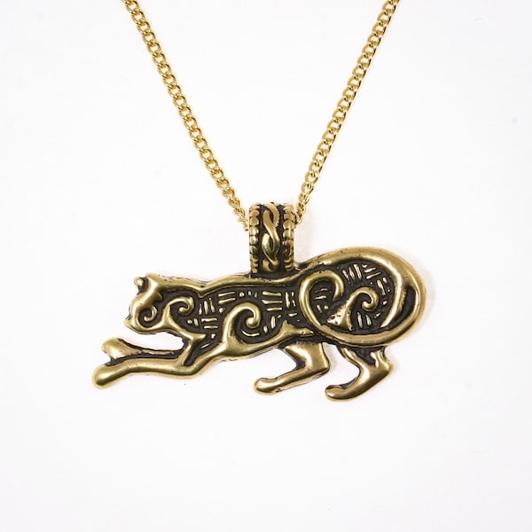Pode incluir: Um colar de ouro com um pingente em forma de animal estilizado com detalhes intrincados. O pingente é feito de latão e tem uma pátina escura.