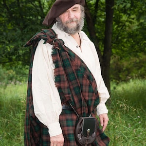 May include: A man wearing a brown hat and a white shirt with a brown and green plaid kilt. He is wearing a brown leather sporran with a fringe.