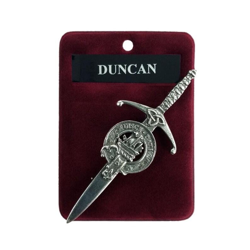 May include: A silver pewter kilt pin featuring a sword and a circular crest with the text "DISCE PATI", "Duncan" is printed on a black label.