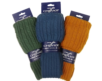 Op de afbeelding: Drie paar gebreide wollen sokken in groen, blauw en oranje. Elke sok heeft een kabelbreipatroon en is gelabeld met "House of Cheviot Merino Wool Blend Made in Scotland."