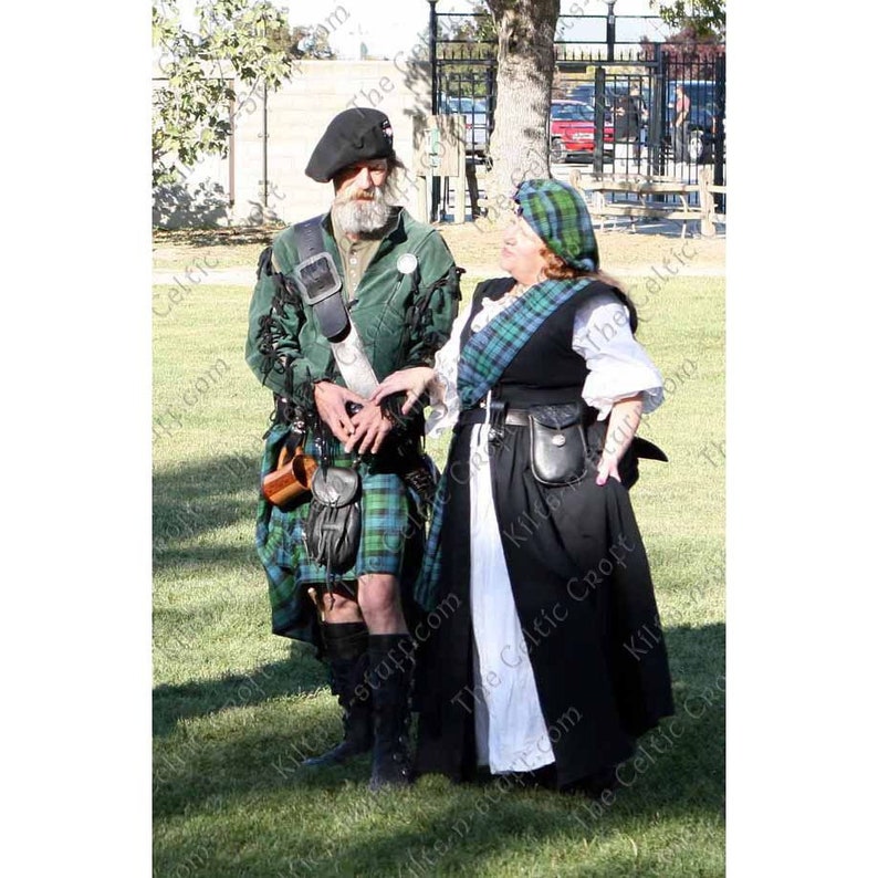 May include: A man and a woman wearing traditional Scottish kilts and clothing. The man is wearing a green kilt with a black sporran and a green jacket. The woman is wearing a black kilt with a white apron and a green jacket. They are both standing on a grassy field.