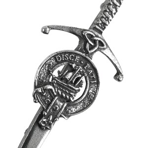 May include: A silver-toned kilt pin featuring a sword design with a Celtic knot and a circular crest with the text "DISCE. PATI."