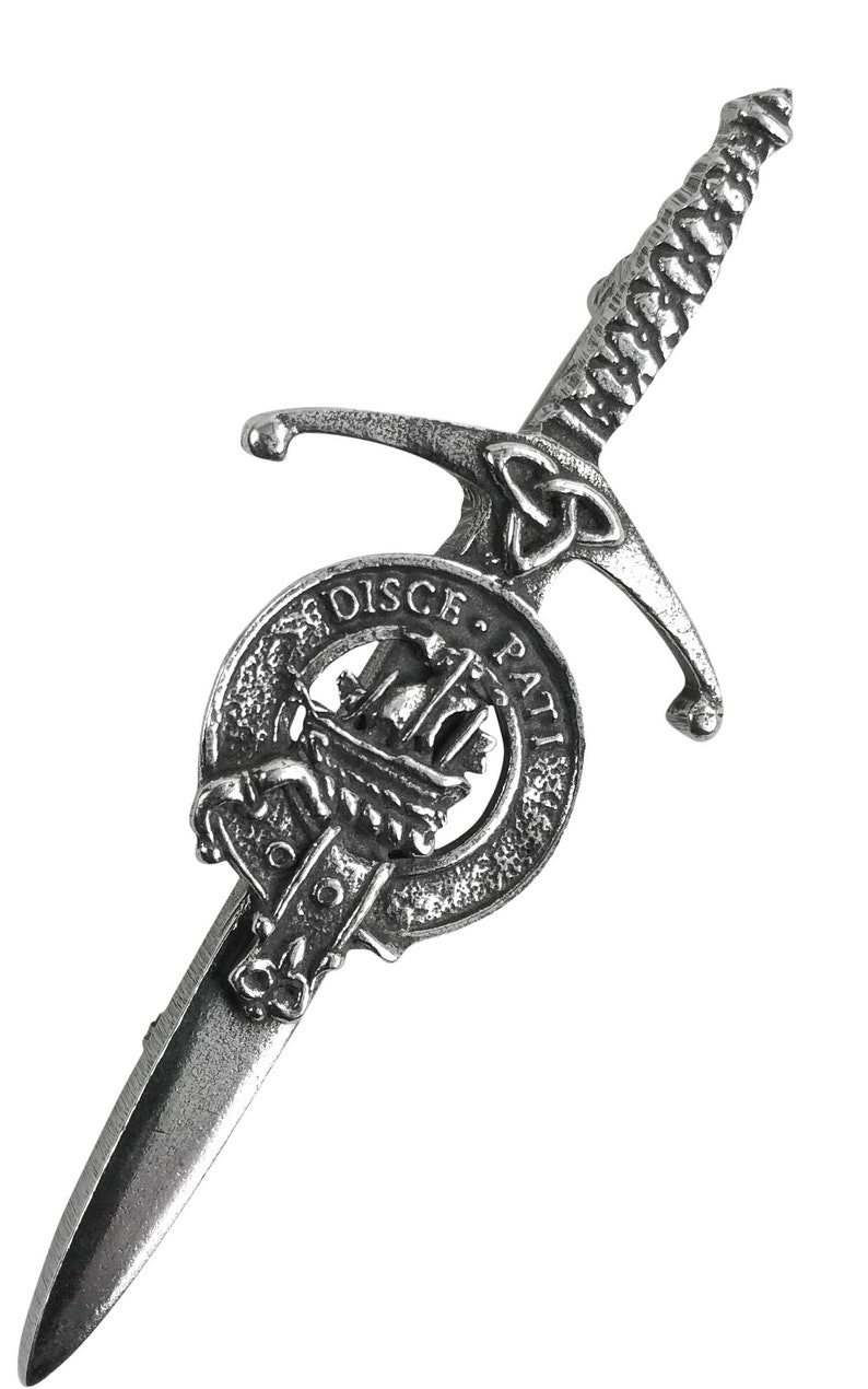 May include: A silver-toned kilt pin featuring a sword design with a Celtic knot and a circular crest with the text "DISCE. PATI."