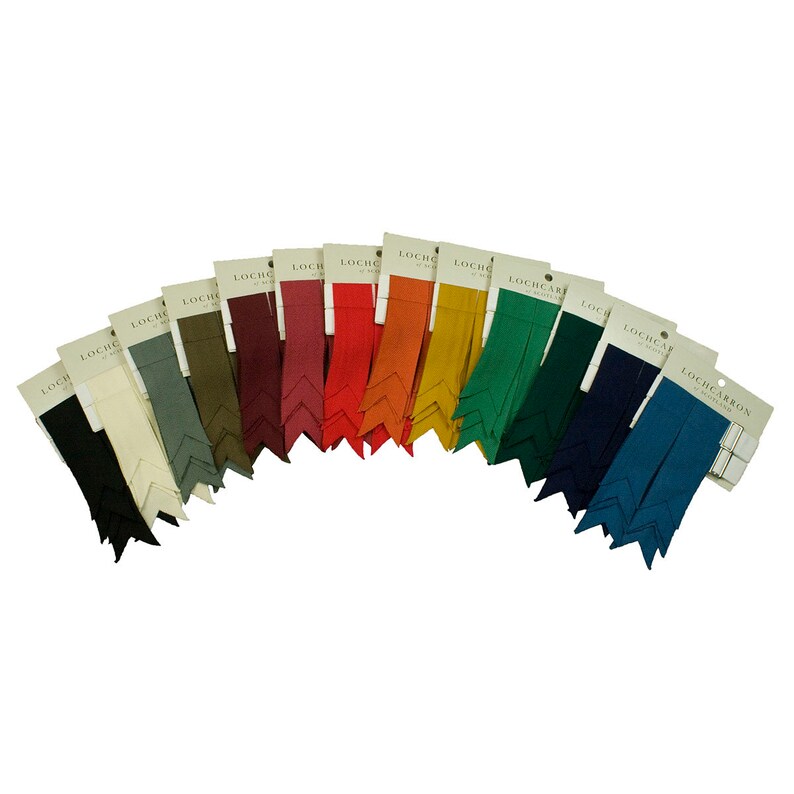 May include: Assortment of 15 kilt hose flashes in various colors, including black, white, gray, green, red, orange, yellow, blue, and teal. Each flash is packaged individually with a white label that reads "LOCHCARRON OF SCOTLAND".