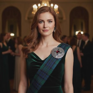 May include: A woman wearing a dark green velvet dress and a tartan sash. A silver brooch with a red center stone is pinned to the sash. The background shows a formal event with chandeliers.