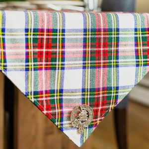 May include: A white tablecloth with a red, green, and yellow plaid pattern. A silver metal clan crest with a lion is attached to the corner of the tablecloth.