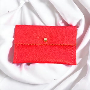 May include: A bright red leather wallet with a gold button closure. The wallet has a scalloped edge and a textured surface.
