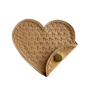 May include: A heart-shaped, tan leather coin purse with a detailed embossed pattern. The purse features a decorative stitched border and a flap secured by a brass snap. The design is a mix of geometric and floral elements.