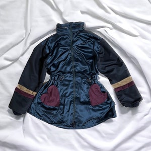 May include: A blue satin jacket with black sleeves and a brown and beige stripe. The jacket has two burgundy heart-shaped pockets on the front.