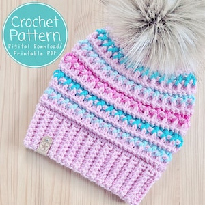 May include: A pink, blue and turquoise crochet beanie with a faux fur pom pom. The beanie has a striped pattern and is made with a soft yarn. The beanie is a crochet pattern, digital download and printable PDF.