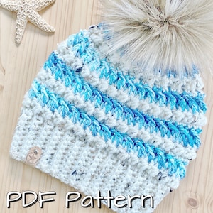 May include: A white and blue crocheted beanie with a fluffy white pom pom. The beanie has a striped pattern with blue and white yarn. The beanie is a crochet pattern.