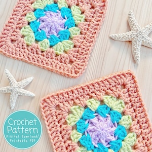 Peut inclure: Deux carrés de grand-mère au crochet avec un centre coloré dans des tons de vert, bleu et violet. Les carrés sont faits avec un fil de couleur pêche et sont disposés sur une surface en bois clair. Le texte "Crochet Pattern Digital Download/Printable PDF" est dans un cercle bleu.