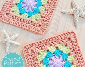 May include: Two crocheted granny squares with a colorful center in shades of green, blue, and purple. The squares are made with a peach colored yarn and are laid out on a light wood surface. The text "Crochet Pattern Digital Download/Printable PDF" is in a blue circle.