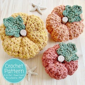 May include: Three handmade crochet pumpkins in shades of yellow, orange, and coral. Each pumpkin has a green crocheted leaf and a small, round, cork-like stem. The pumpkins are arranged on a light wood surface with two starfish. The image includes the text "Crochet Pattern".
