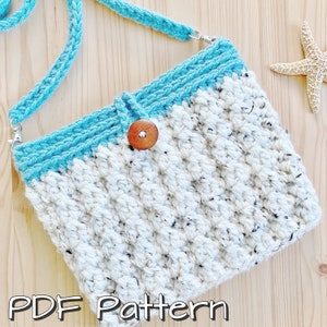 May include: A crocheted bag with a white and blue colour scheme. The bag has a long strap and a wooden button. The bag is on a wooden surface. PDF Pattern.
