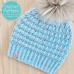 May include: A light blue crochet beanie with a white faux fur pom pom. The beanie has a speckled pattern and is made with a soft yarn. The beanie is a crochet pattern, digital download, and printable PDF.