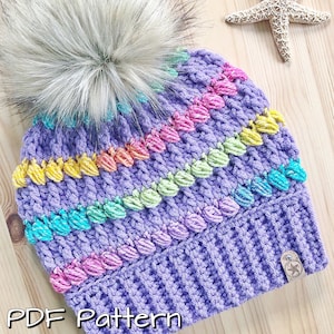 May include: Purple crochet beanie with a rainbow stitch pattern and a fluffy white pom pom. The beanie has a "PDF Pattern" label at the bottom.