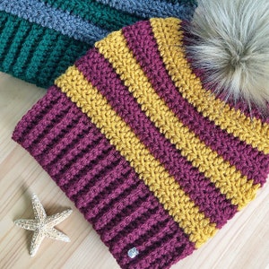 May include: A burgundy and gold striped crocheted beanie with a fluffy white pom pom on top.