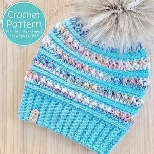 May include: A crochet pattern for a blue and white striped beanie with a fluffy pom pom. The pattern is a digital download and includes instructions for crocheting the hat.