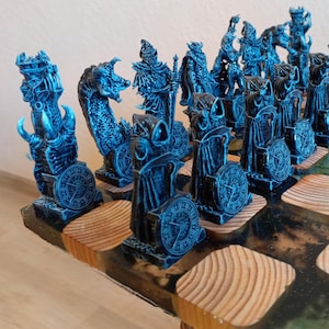 Puede incluir: Un juego de ajedrez azul y negro con piezas esculpidas detalladas sobre un tablero de madera con un acabado de resina epoxi verde oscuro y marrón.