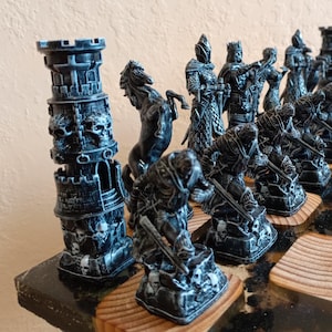 Può includere: Un set di scacchi nero e argento con un castello, cavalieri e altri pezzi disposti su una scacchiera di legno.