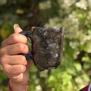 May include: A black and green mug with a marbled design. The mug has a handle and is made of a smooth, polished material.