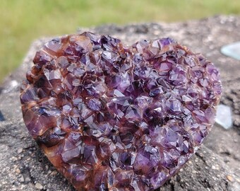 May include: A heart-shaped amethyst crystal cluster with a purple and brown colour. The crystal is made up of many small, pointed crystals.