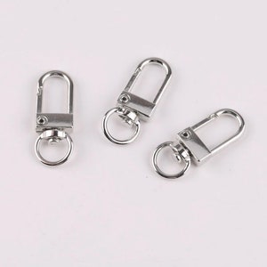 May include: Three silver swivel snap hooks with a round ring on each. The hooks are commonly used for attaching keychains, bags, or other accessories.