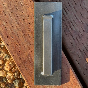 May include: A black metal door handle with a rectangular shape and a long, narrow pull.