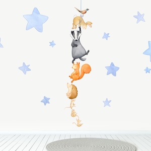 May include: A watercolour illustration of a woodland animal mobile with a badger, squirrel, hedgehog, and mice hanging from a string with blue stars in the background.