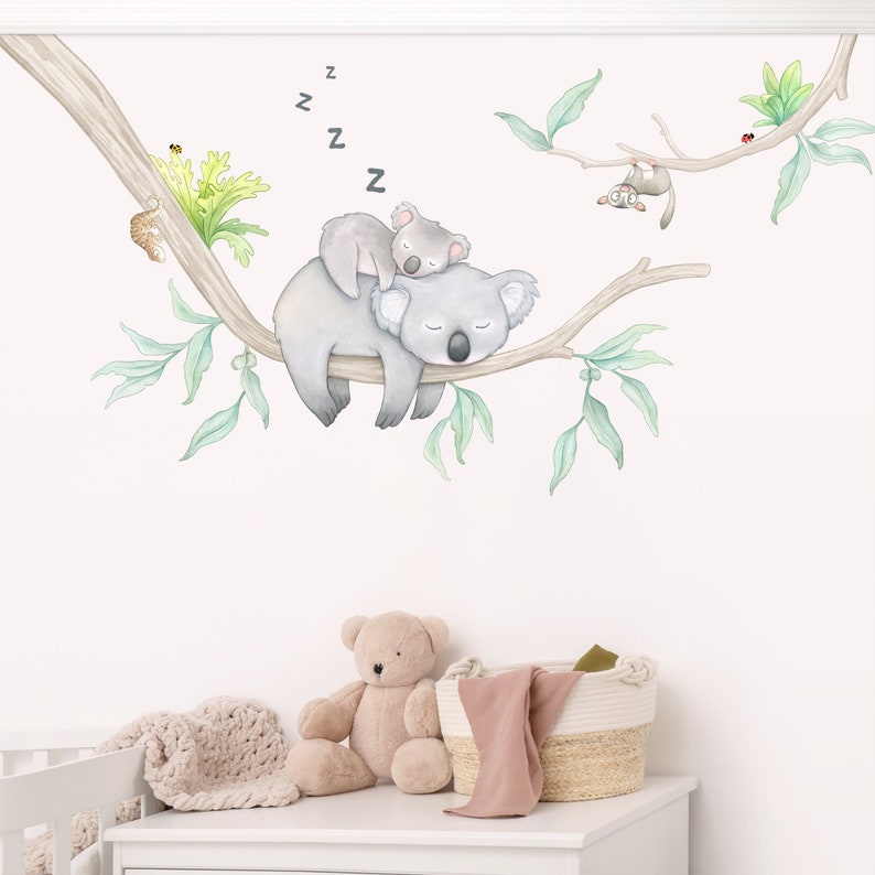 May include: A watercolor illustration of two koalas sleeping on a tree branch with green leaves. The koalas are gray and white, and the leaves are a light green. There are also two small birds and a ladybug on the branch. The illustration is on a white background.